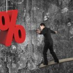 Businessman balancing on wooden board with red percentage sign